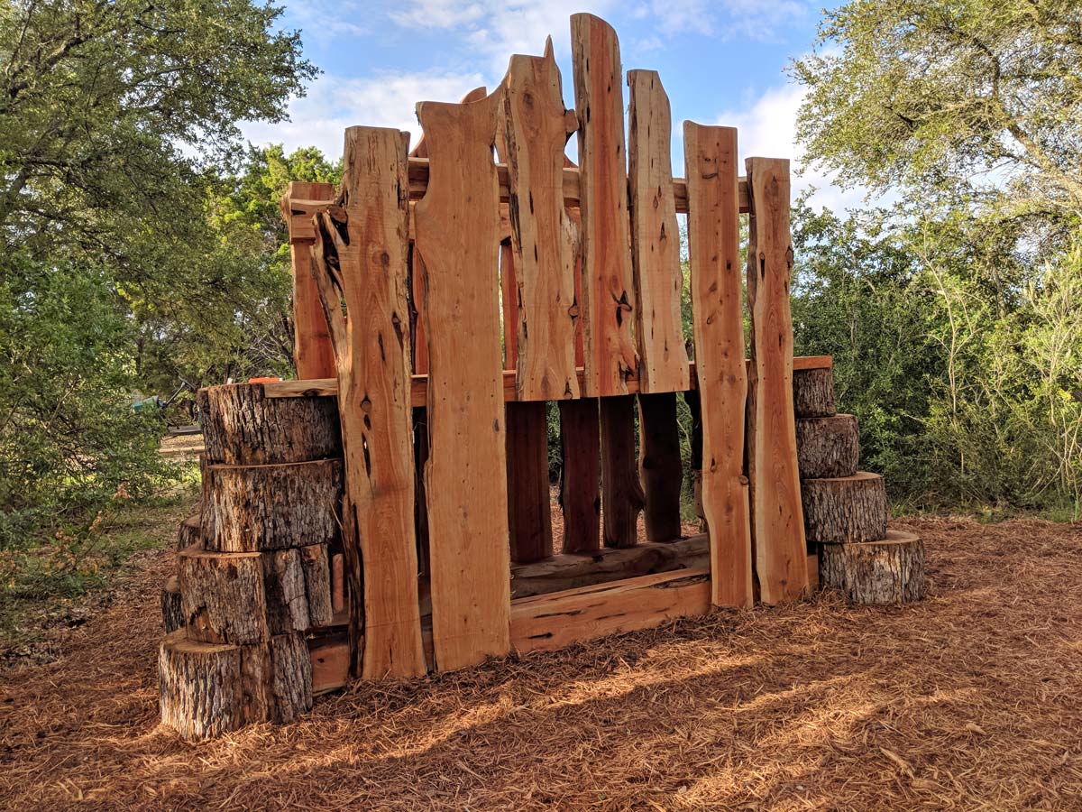 A fort made of segments of oak arranged in a basic house pattern stands in the middle of a clearing.