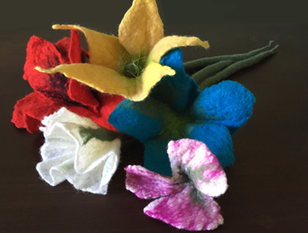 Colorful felt flowers made by hand are laid out against a black background.