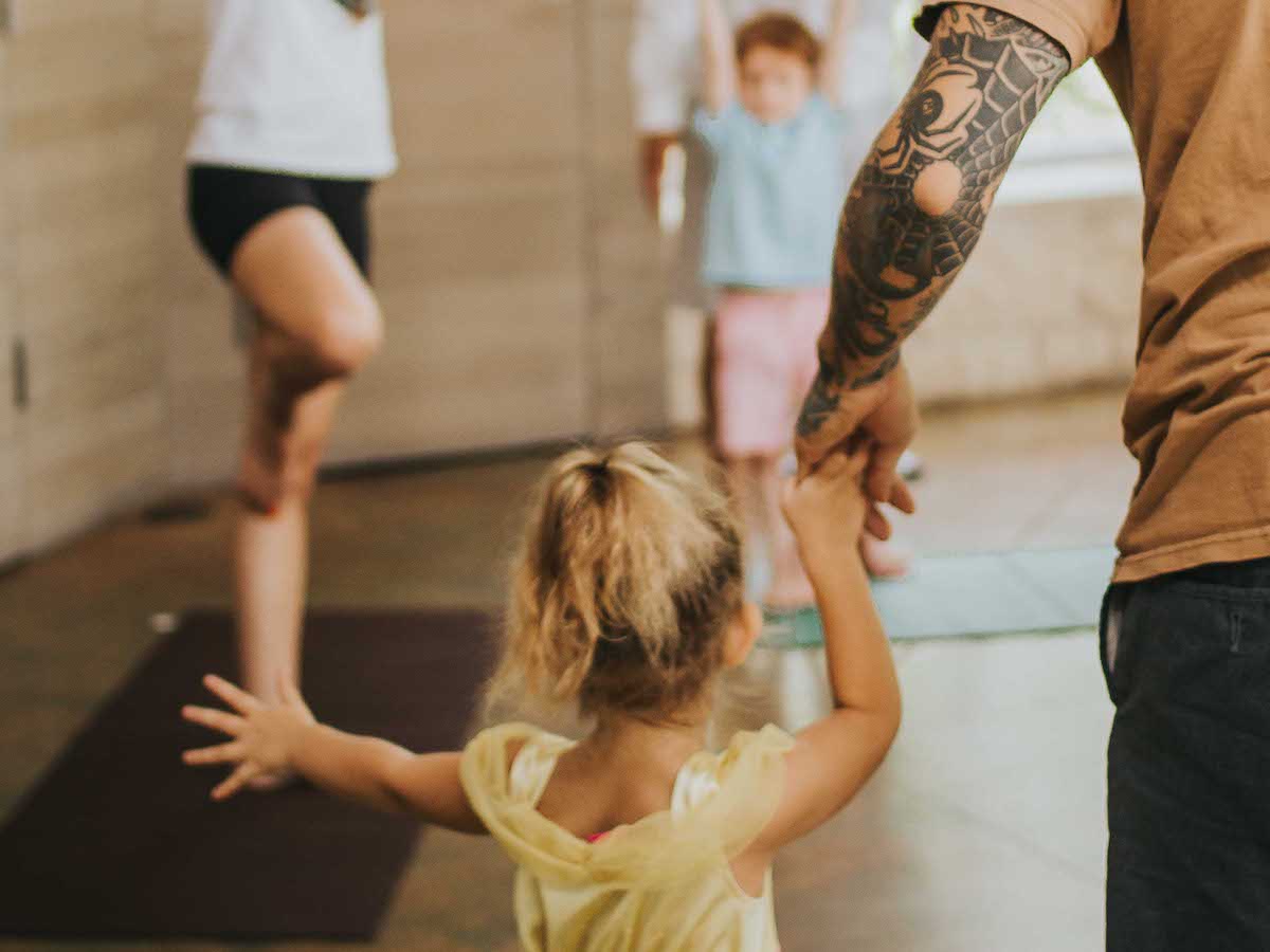 A young girl does the tree pose on a yoga mat with her parents.