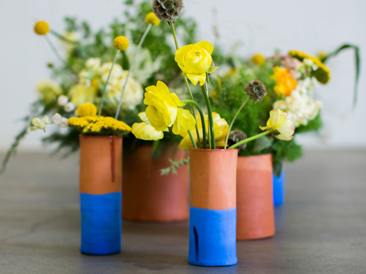 A group of ceramic planters filled with wildflowers sits on the concrete. Some of the planters have a blue-glaze design around the bottom half.