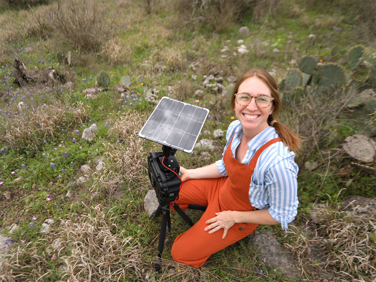 A Jha Lab researcher works in the field; she is smiling at the camera.