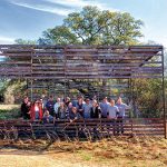 A group of workers and researchers gather under a wooden trail structure that has been contructed in the middle of a prairie trail.