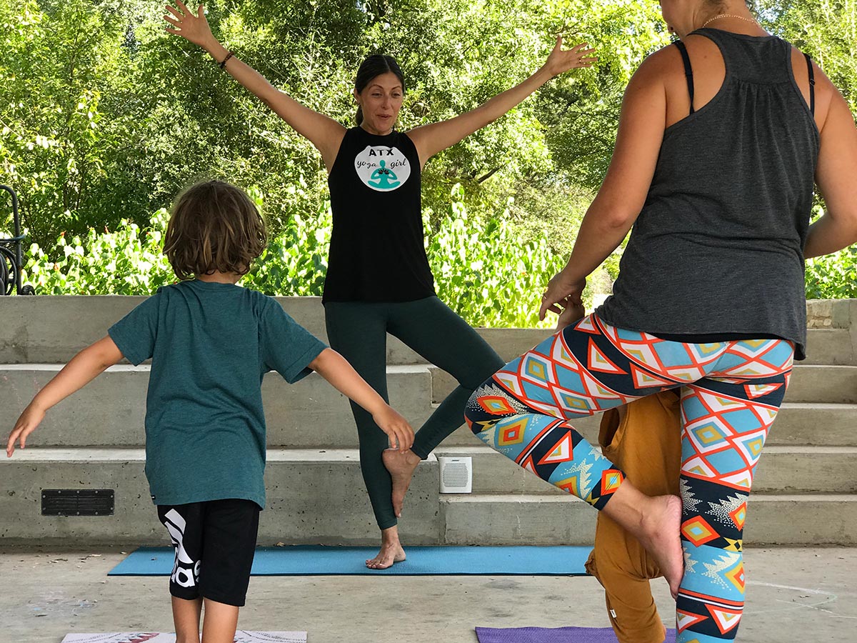 A parent and child follow a yoga instructor as she leads them through a series of poses.