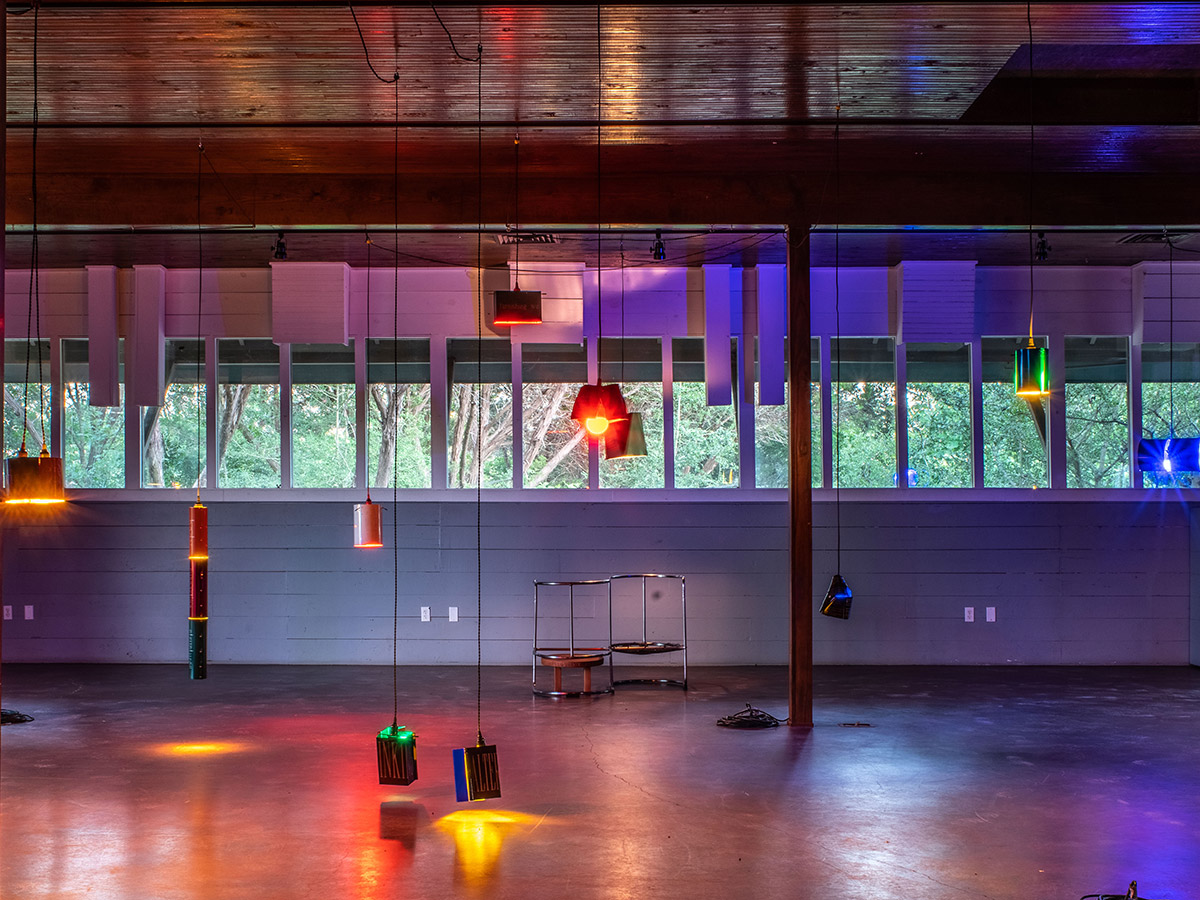 An art installation featuring several hanging light fixtures attached to the ceiling, shining beams of colorful light across the room.