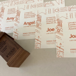 A wooden award shaped like the UT tower lies next to a series of paper certificates with burnt orange text on white.