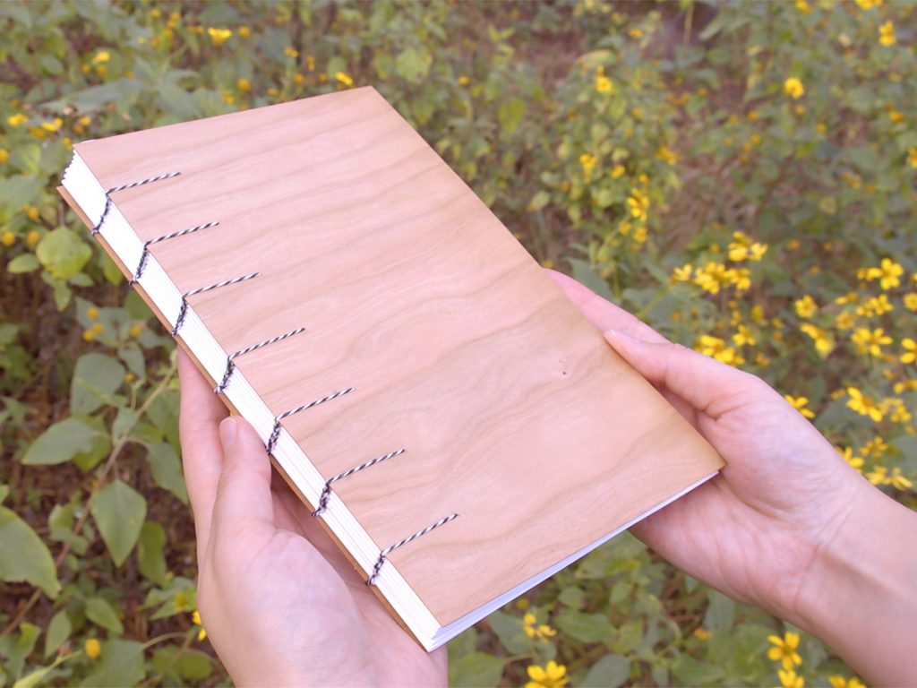 A hardbound book with an unfinished wood cover and black and white stripped sting binding it.